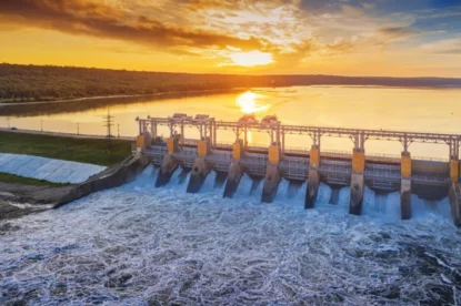 Imagem mostra vista de usina hidrelétrica com reservatório e pôr do sol ao fundo.