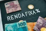 Palavra Renda Fixa escrita em um quadro com letras rodeado de cédulas e moedas do real brasileiro. Dinheiro, Brasil, investimentos, Tesouro Direto.