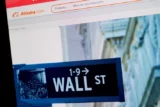Tela de computador com a logo da empresa chinesa Alibaba com imagem da placa de Waal Street, onde fica a bolsa de Nova York.