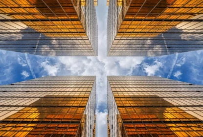 Vista de baixo para cima de arranha-céus espelhados em metrópole, com reflexo de nuvens entre edifícios altos, vidros de construção, negócios e finanças.