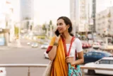 Jovem indiana usando sari fala no celular em rua de cidade na Índia.