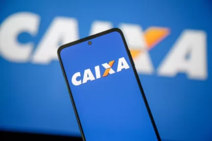 Celular com logomarca da Caixa Econômica Federal e fundo azul. Atrás do celular, há um telão com a mesma imagem.