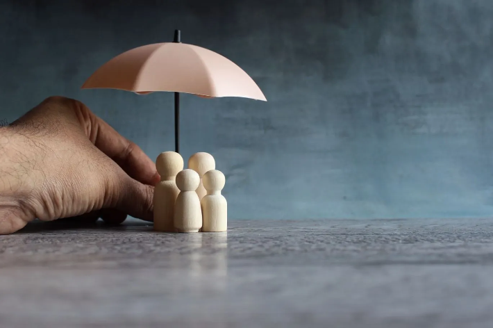 Seguro de vida: imagem mostra guarda-chuva protegendo família de bonecos de madeira em miniatura.