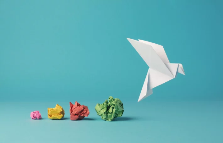 Bolas de papel amassadas coloridas em sequência com pomba de papel ao final, que se refere a oportunidades presentes nos investimentos. (Imagem: Andreas Berheide em Adobe Stock)