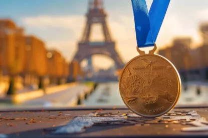 Foto mostra uma medalha de ouro das Olimpíadas; ao fundo a Torre Eiffel, símbolo da capital francesa, Paris.