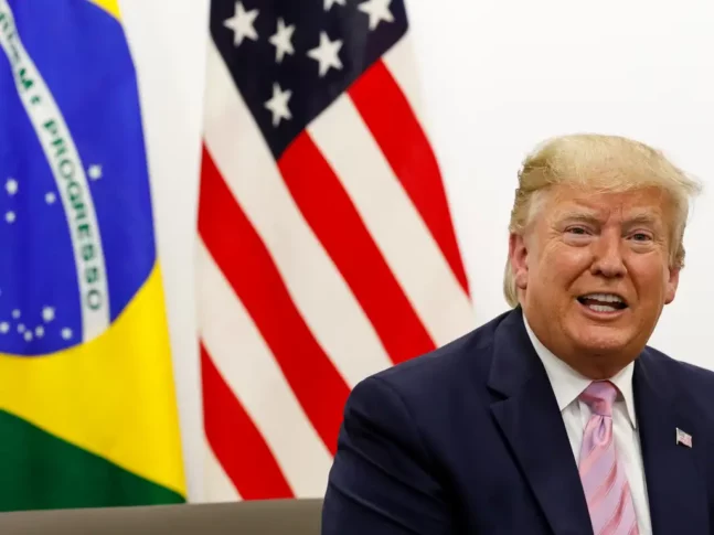 Retrato de Donald J. Trump, ex-presidente dos Estados Unidos, com bandeiras de seu país e do brasil ao fundo, durante visita a Osaka, no Japão.