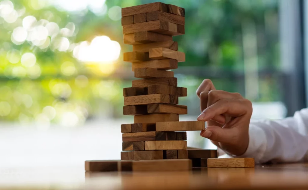 Mão de garota tenta arrancar bloco de madeira sem derrubar a torre de Jenga. Conceito de risco de negócios.