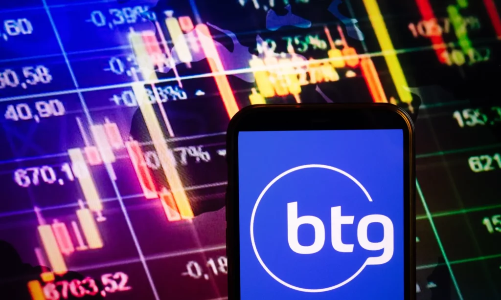 Aplicativo do BTG Pactual contra tela com gráfico do mercado financeiro.