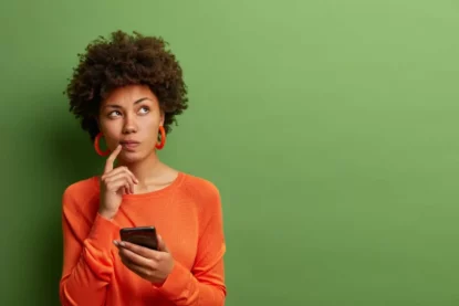 Mulher em dúvida, com o celular na mão.