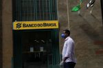Homem andando de máscara em frente ao Banco do Brasil.