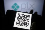 Imagem mostra em primeiro plano um QR Code em uma tela celular e, ao fundo, a logomarca do Pix