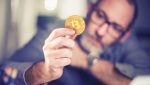 Homem segura uma moeda fictícia de bitcoin