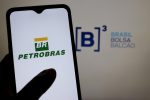 Mão segura smartphone com o logo da Petrobras. Ao fundo, logo da B3