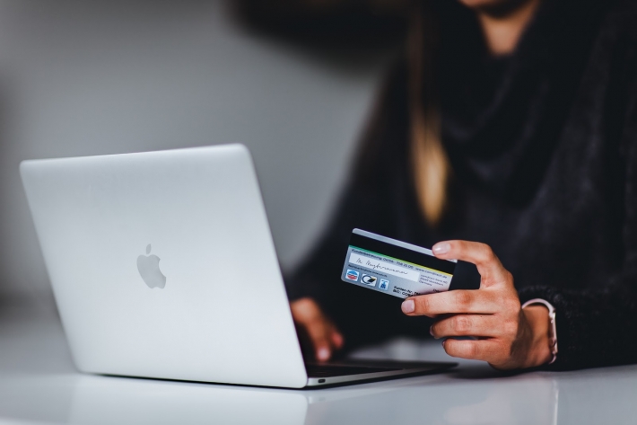 Mulher segura cartão de crédito enquanto usa laptop