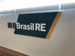 Parede com a a logo do IRB Brasil estampada: IRB em verde com fundo branco e Brasil RE em branco sobre um retângulo verde com uma borda em amarelo.
