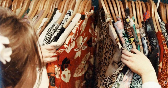 Mulher olhando arara com diversas roupas em cabides
