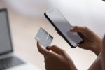 Imagem de mãos segurando um celular e um cartão de crédito.
