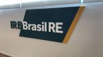 Parede com a a logo do IRB Brasil estampada: IRB em verde com fundo branco e Brasil RE em branco sobre um retângulo verde com uma borda em amarelo.